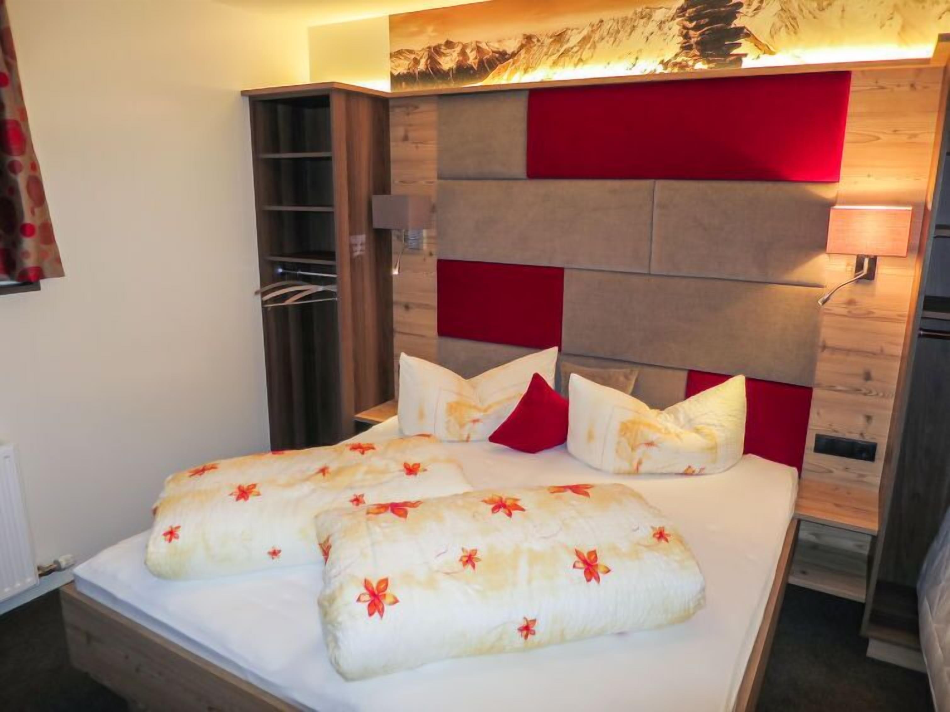 A hotel room with a bed, a wardrobe, a mirror, and a wall-mounted lamp.