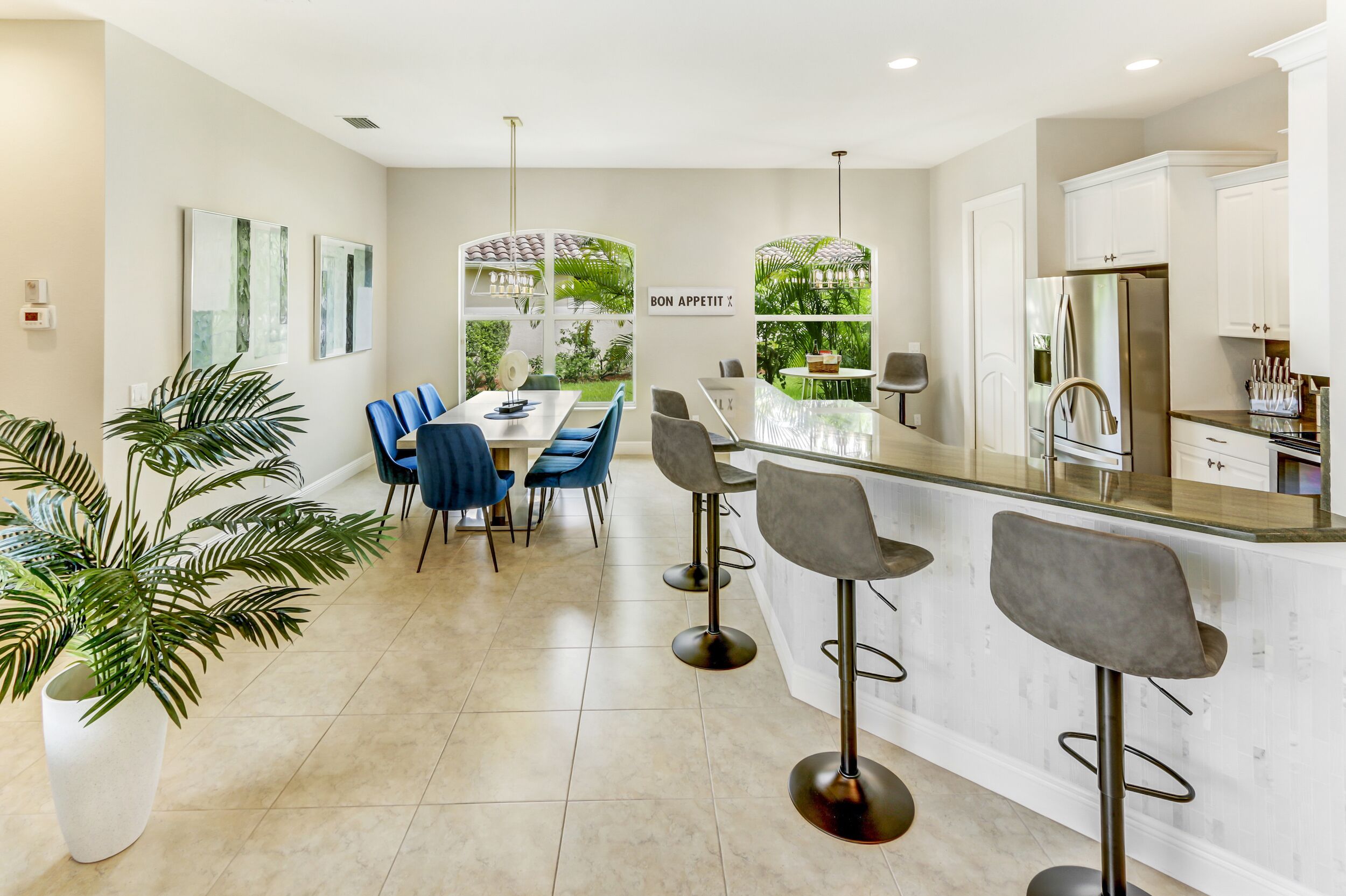 A modern kitchen with a central island, bar stools, and a dining area with blue chairs.