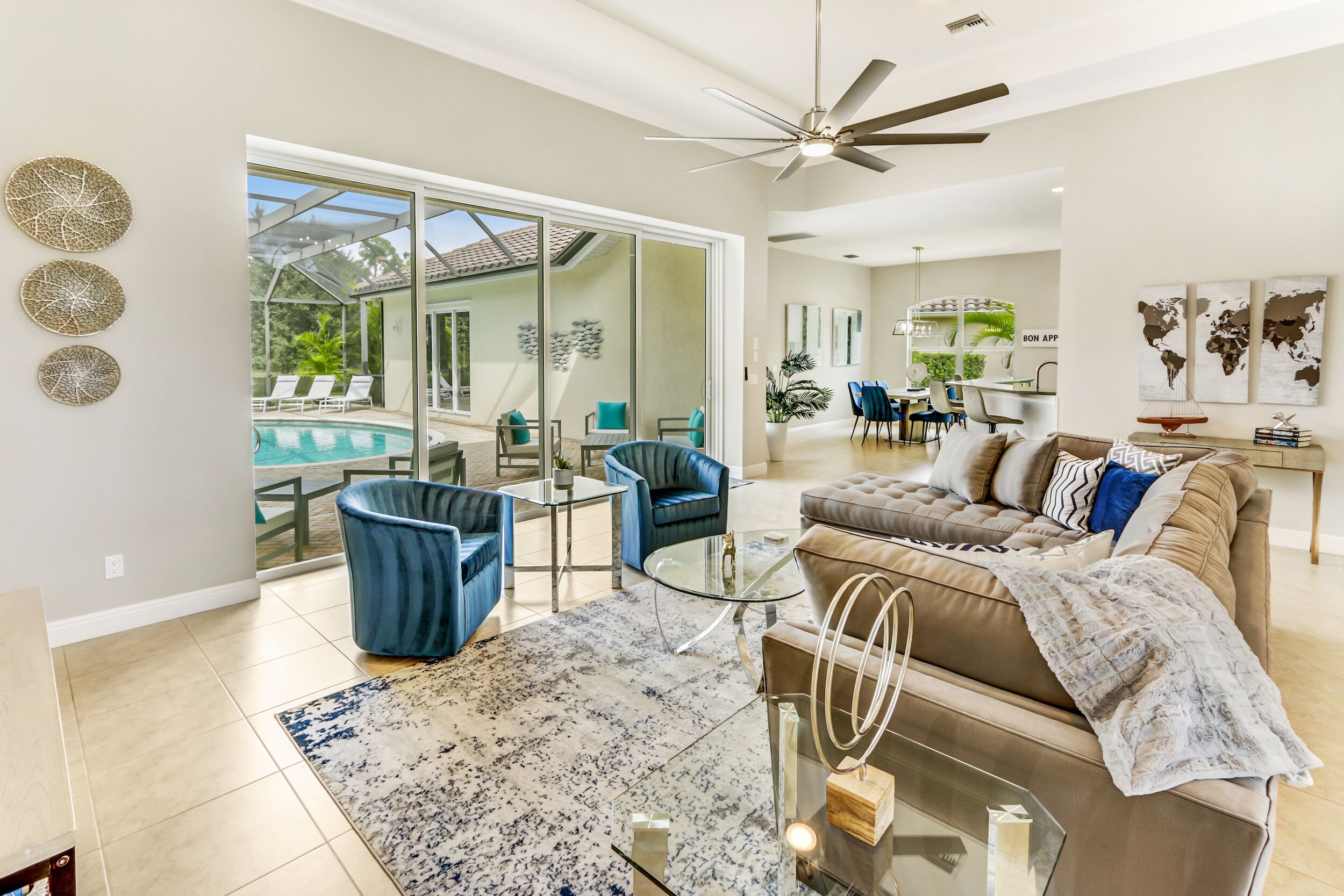 A spacious living room with a large glass door leading to a pool area, a ceiling fan, and a dining area with a view of the pool.