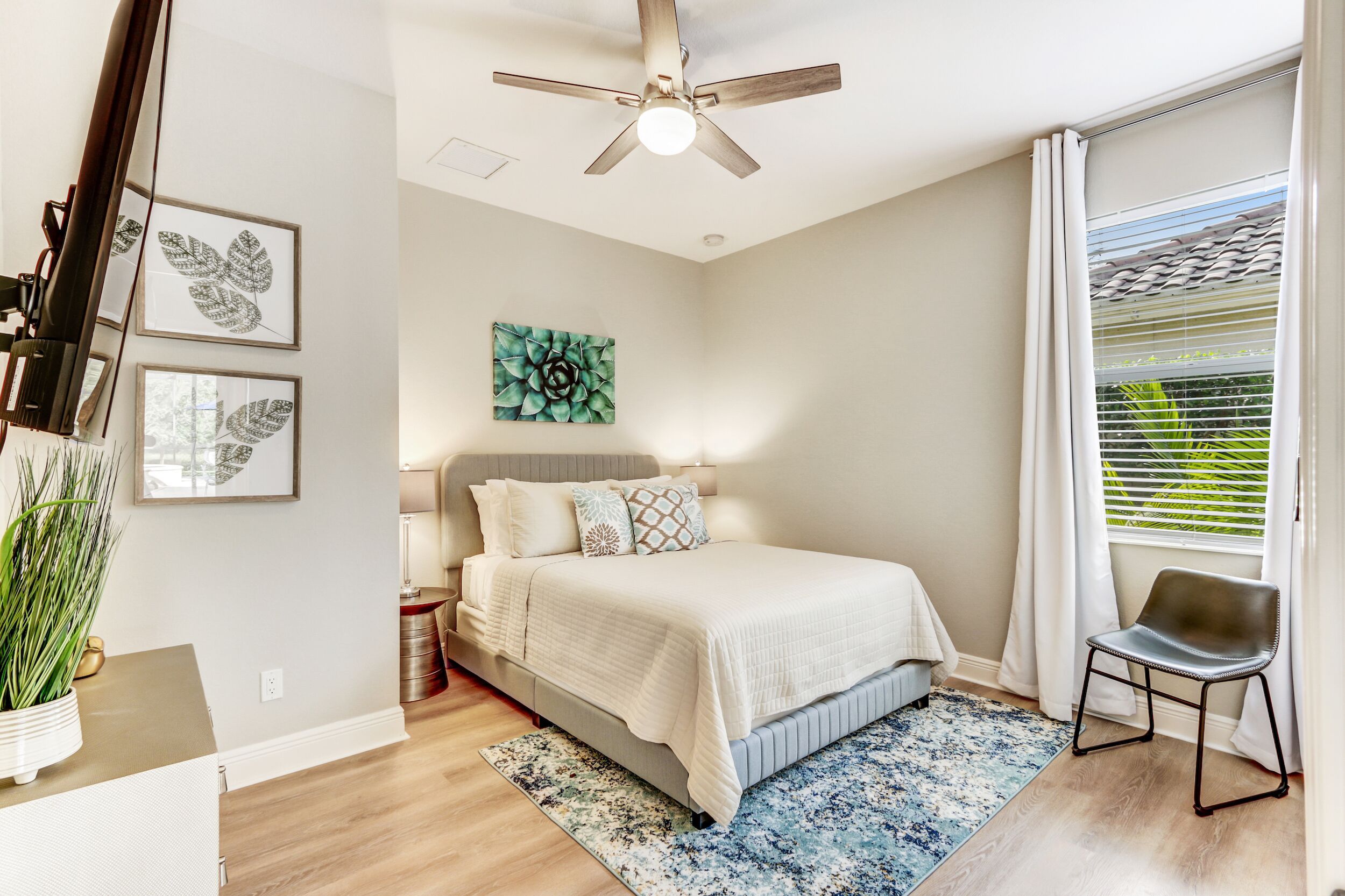 Un dormitorio con cama, ventilador de techo, ventana con persianas y decoración en la pared.
