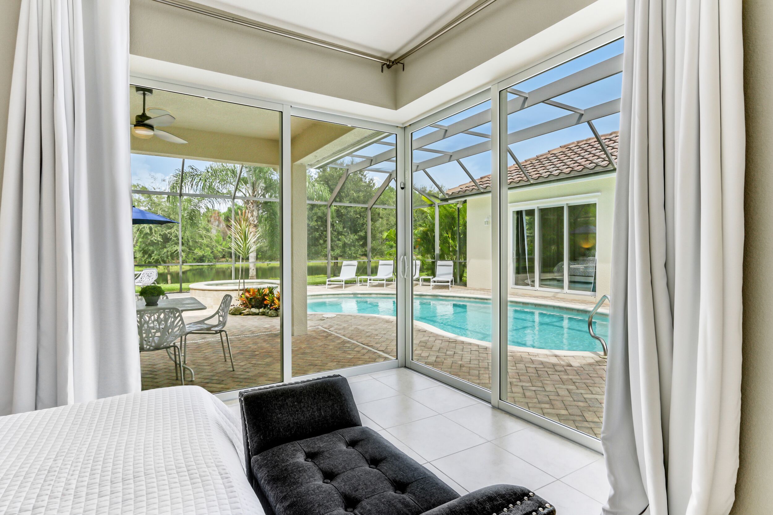 A room with a large sliding glass door leading to an outdoor swimming pool area, a bed, and a seating area with a table and chairs.