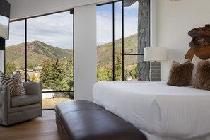 A bedroom with a large window, a bed, a chair, and a lamp.