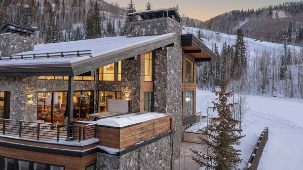 A modern ski resort building with a stone facade, large windows, and a wooden deck area.