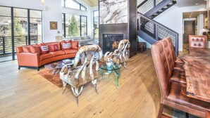 A spacious living room with a fireplace, a leather sofa, a glass coffee table, and a wooden dining table.