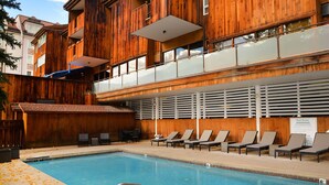 A wooden building with a pool, lounge chairs, and a sign indicating pool rules. - Lionshead Center | 4BR Penthouse, Steps to Gondola (Vail)