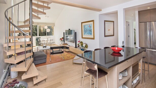 A modern kitchen with a central island, a dining area with chairs, a staircase, and a living room with a sofa and coffee table. - Lionshead Center | 4BR Penthouse, Steps to Gondola (Vail)