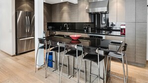 A modern kitchen with stainless steel appliances, a central island with bar stools, and a sleek design. - Lionshead Center | 4BR Penthouse, Steps to Gondola (Vail)