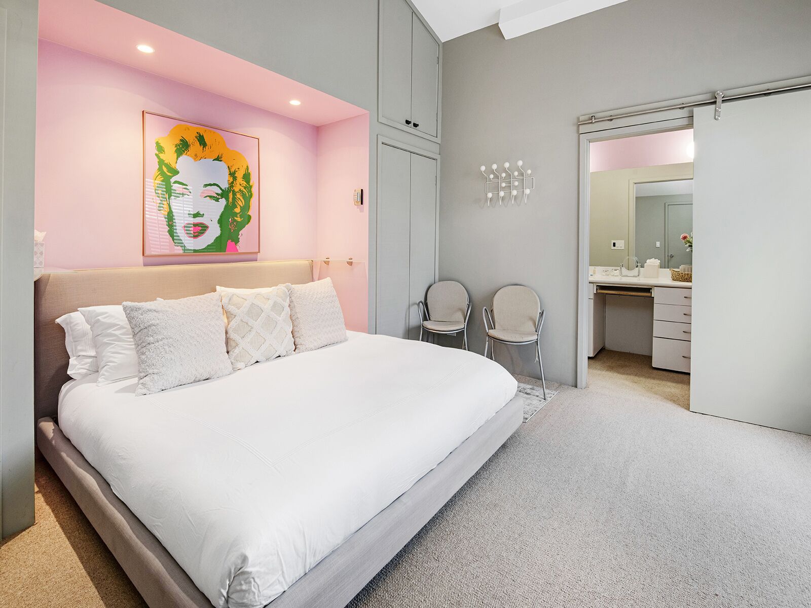 A bedroom with a large bed, a painting on the wall, and a bathroom visible through an open door.
