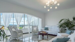 Un salon spacieux avec une grande fenêtre, des meubles blancs et un lustre.