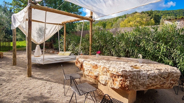 Un espace extérieur aménagé dans un style rustique, avec une balançoire en bois, un banc en pierre et des chaises en métal.