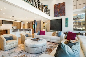 A spacious living area with a high ceiling, a kitchen with wooden cabinets, and a dining area with a large window.