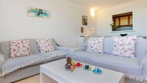Sala de estar com dois sofás cinzas, cada um com almofadas florais, uma mesa de centro branca com um aviso e um quadro na parede.