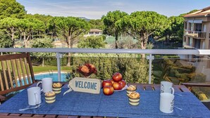 Uma varanda com uma placa de boas-vindas, uma mesa com canecas e doces, e vista para uma piscina e vegetação.