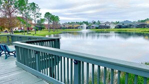 A wooden deck with blue chairs overlooking a calm lake, surrounded by residential buildings. - 3BR Townhome Near Disney I Resort Pool, Hot Tub & Disney-Themed Room (Kissimmee)