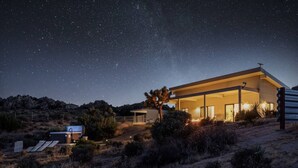 A modern house with a large open patio, surrounded by dry vegetation and a clear night sky.