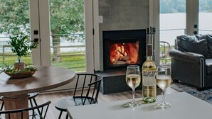 A modern living room with a fireplace, a dining table with chairs, and a view of a lake through large windows.