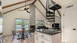 A modern kitchen with a central island, wooden flooring, and a black spiral staircase.