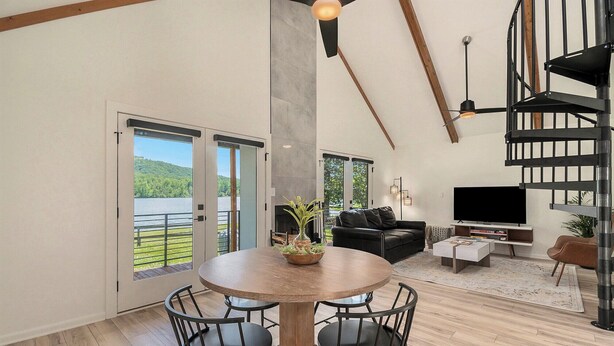 A spacious living area with a dining table, black leather sofa, and a TV.