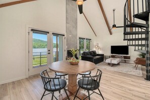 A spacious living area with a dining table, black leather sofa, and a TV.