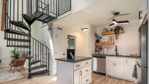 A modern kitchen with a central island, white cabinetry, and a black staircase.