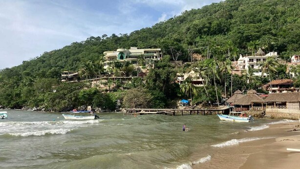 Zona costera con playa, barcos y edificios en una ladera.
