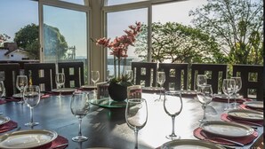 Mesa lista para una comida, con vasos y platos transparentes, una planta en maceta y vista al mar a través de amplias ventanas.