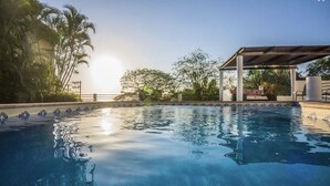 Una piscina con borde de azulejos, rodeada de palmeras y una zona de estar cubierta.