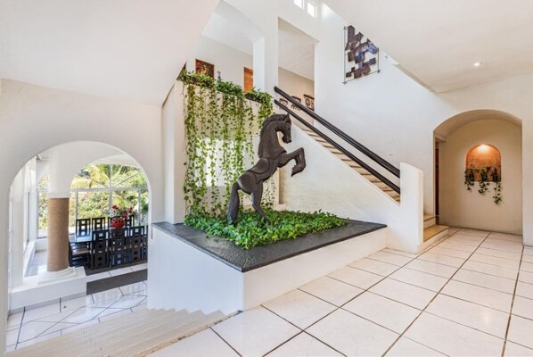 A modern staircase with a horse sculpture, surrounded by greenery, leading to a dining area with outdoor views. - Oceanview FAST WiFi Private Yard Pool Executive Chef Staff Amazing Views (boca de tomatlan)