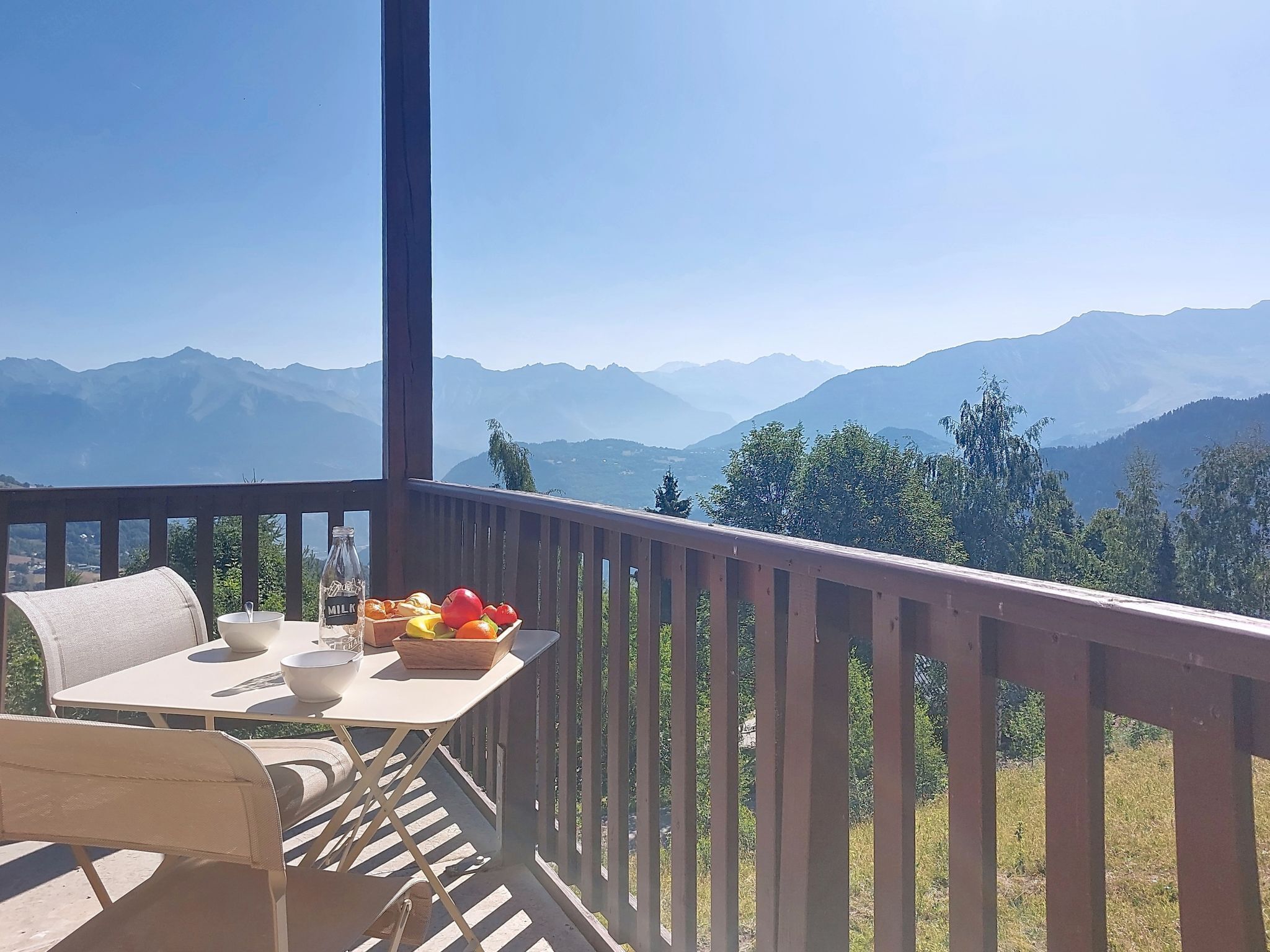 A balcony with a table set for breakfast, overlooking a mountainous landscape.
