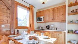Una mesa de comedor de madera dispuesta para seis personas, una cocina con armarios de madera, un microondas y una cafetera.