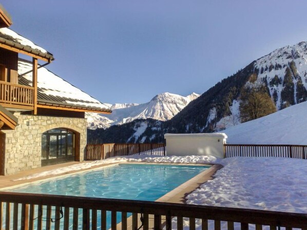 A pool area with a stone building, wooden deck, and a view of snow-covered mountains. - Les Alpages du Corbier by Interhome (Le Corbier)