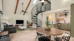 A spacious living area with a modern kitchen, a dining table, and a spiral staircase.