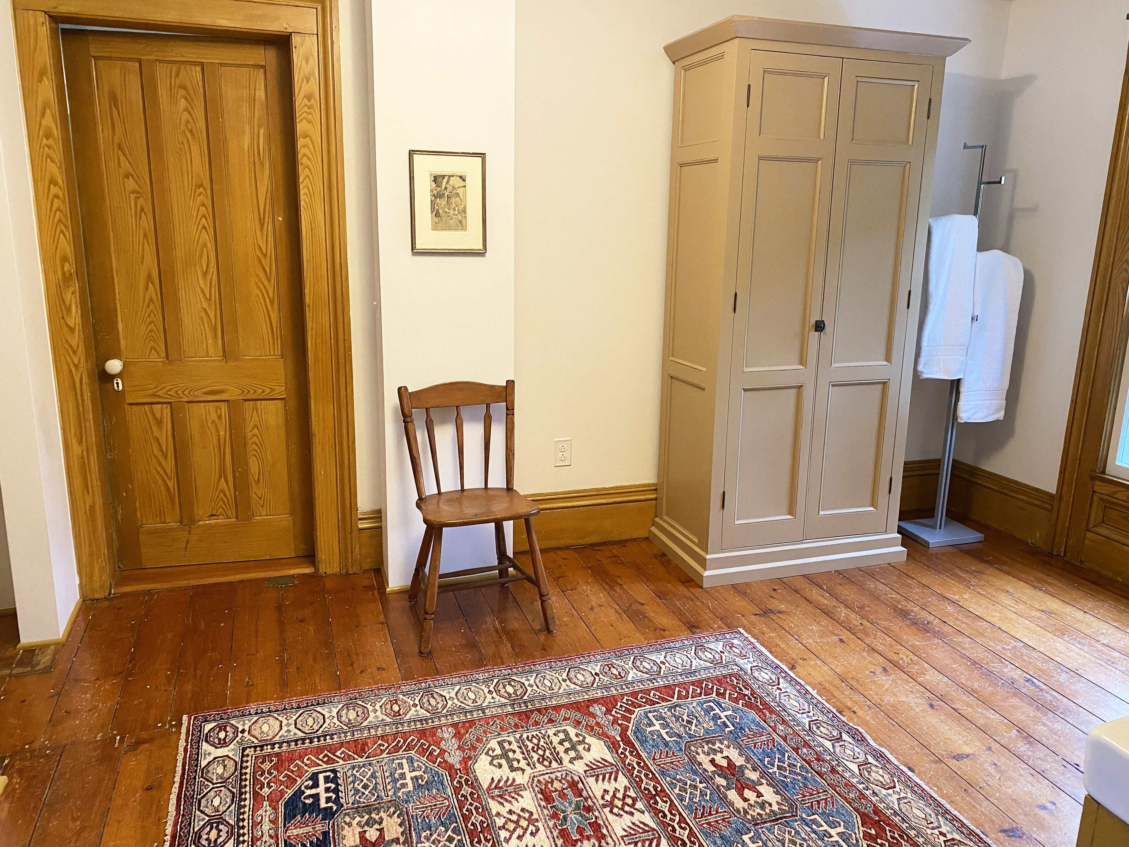 A room with a wooden door, a chair, a wardrobe, and a patterned rug.