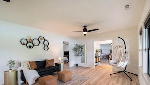 Un salon moderne avec un canapé noir, des poufs marron, un fauteuil suspendu et un plancher en bois.