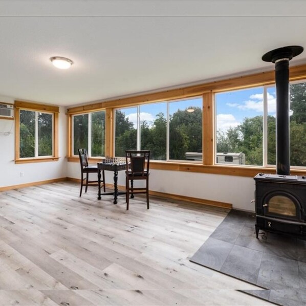 Enjoy a cozy atmosphere in this spacious room with a high ceiling and large windows, featuring a black wood-burning stove and dining area.