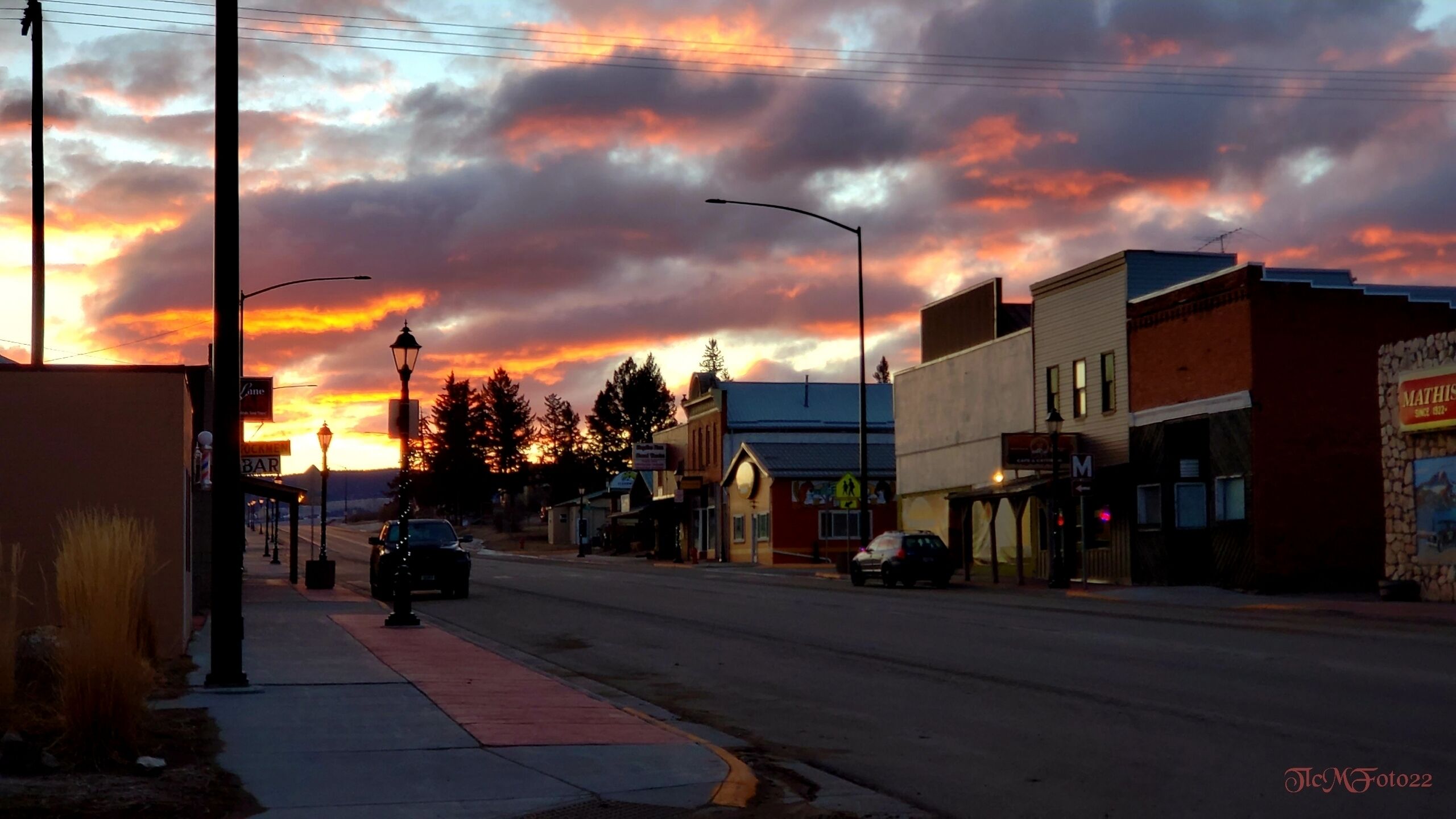 A street view at sunset with buildings, a sidewalk, and a car.