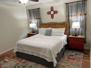 Un dormitorio ordenado con una cama grande, dos mesitas de noche, un cabecero y un elemento decorativo en la pared.
