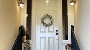Un escalier en bois mène à une porte blanche ornée d’une guirlande, de part et d’autre de laquelle sont fixées deux lanternes murales.
