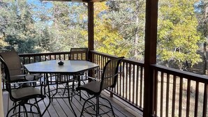 Une terrasse en bois avec une table et des chaises, un ventilateur de plafond et une vue sur les arbres.