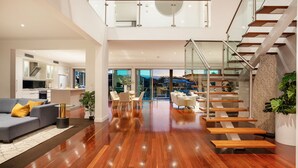 A spacious living area with a wooden staircase, a sofa, and a dining area. - Stunning Waterfront home on the Gold Coast*Heated Pool* 
Pet Friendly. (Surfers Paradise)