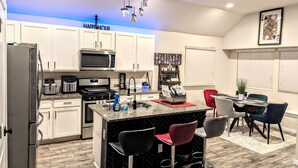 A modern kitchen with white cabinets, a black and white marble island, and a red bar stool.