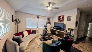 A living room with a sofa, two armchairs, a coffee table, a TV, and a ceiling fan.