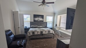 A bedroom with a bed, a desk, a chair, a ceiling fan, and a window.