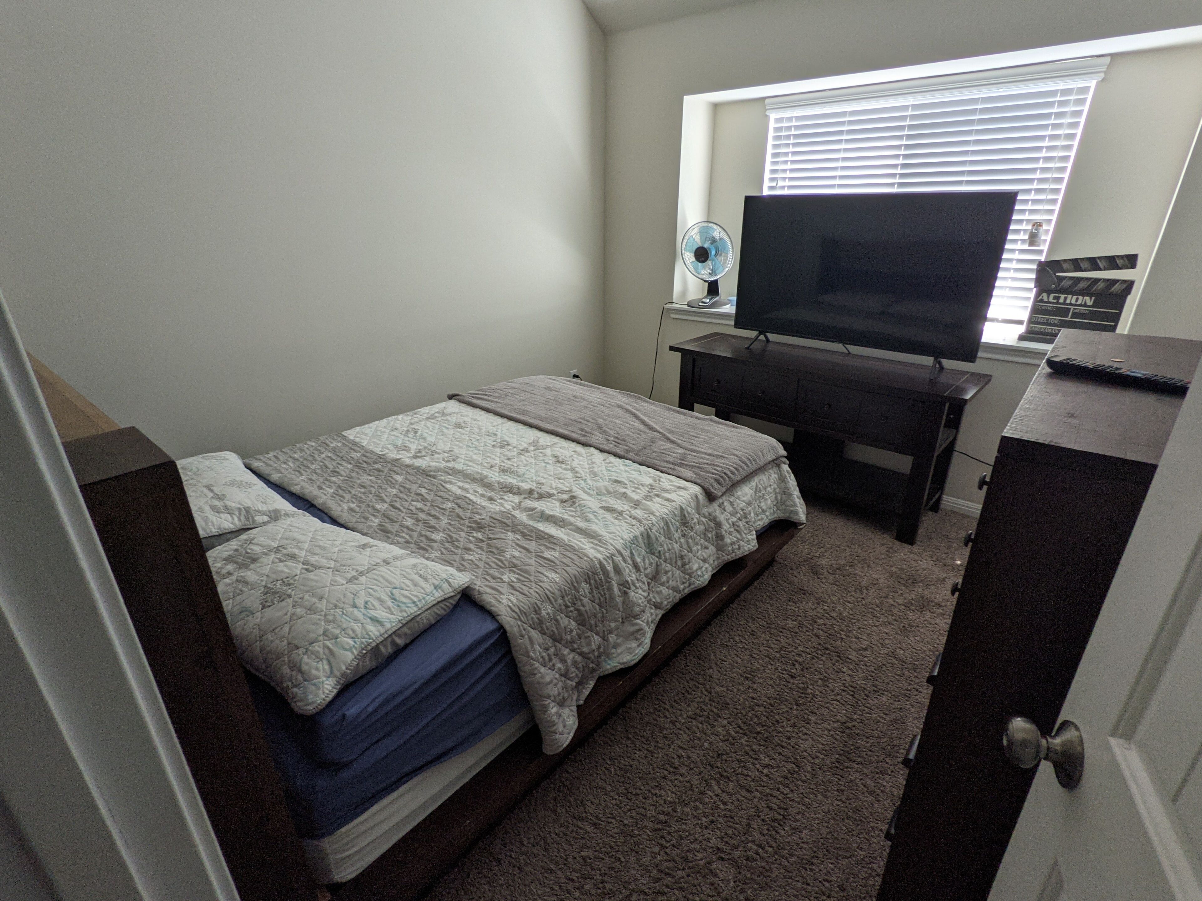 A bedroom with a bed, a TV, a dresser, and a window with blinds.