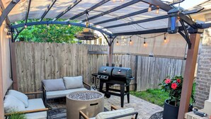 A covered patio area with a grill, seating, and a fire pit.