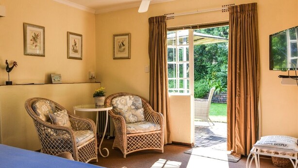 A room with a bed, two wicker chairs, a small table, a TV, and a view of greenery outside.