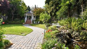 Un jardín con un pabellón, un sendero de piedra y un pequeño arroyo.