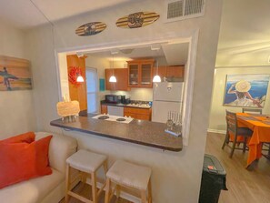 Une cuisine compacte dotée d’un îlot central, de tabourets en bois et d’un coin repas avec des nappes orange.