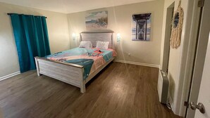 Ein Schlafzimmer mit einem Bett, einem Nachttisch, einer Wandlampe, einem Gemälde und einer Tür.