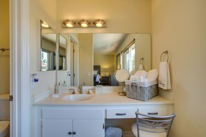 Une salle de bain avec un lavabo blanc, un miroir et une commode avec des tiroirs. Des serviettes sont accrochées au mur et un panier est posé sur la commode.